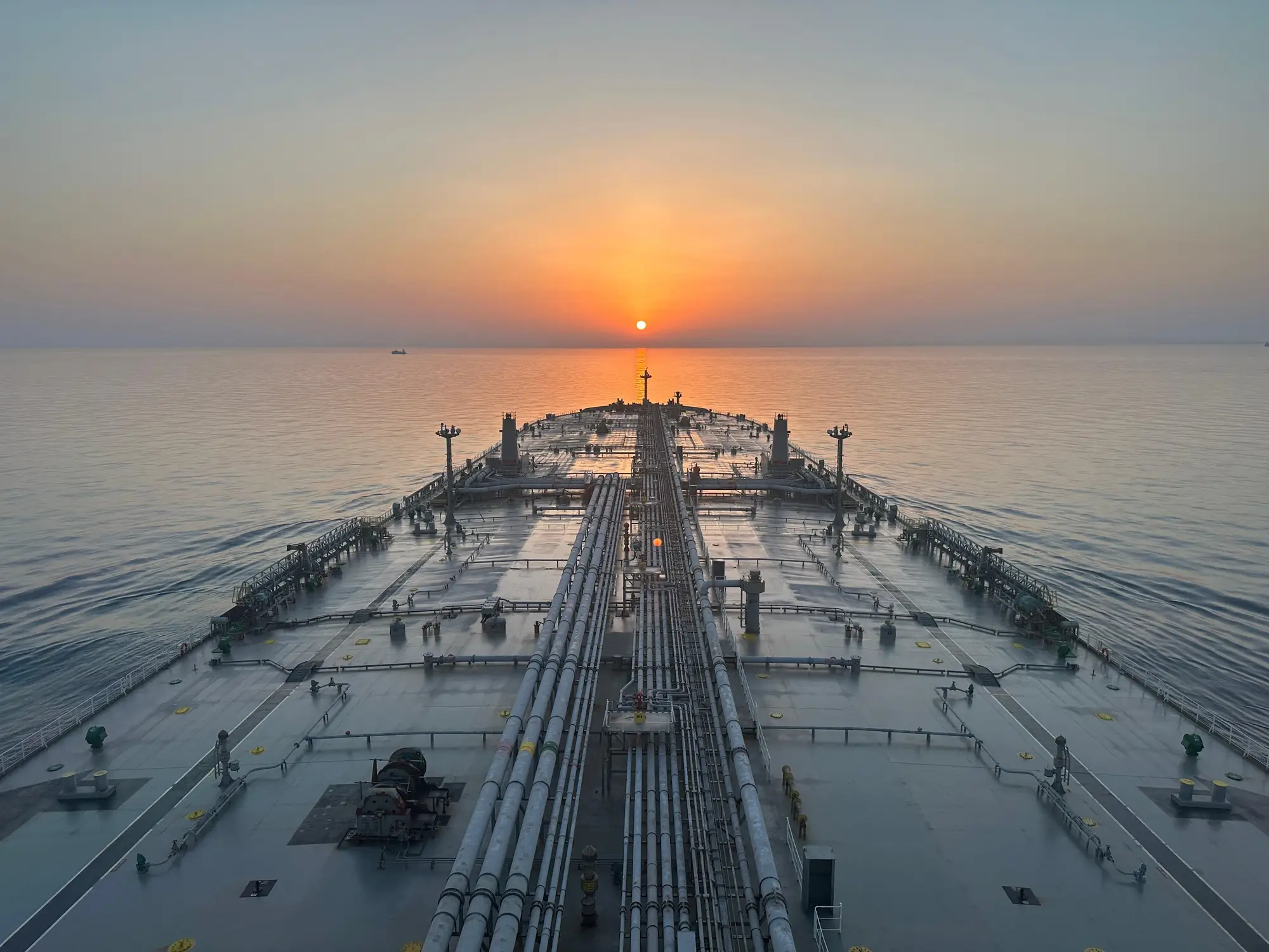 The long main deck of a tanker running towards a low sun on a flat sea